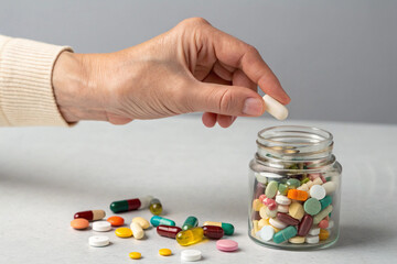 Closeup of a human hand selecting a white pill from a jar filled with colorful medication, vitamins, and supplements, symbolizing healthcare, treatment, wellness support, pharmaceutical choice, 