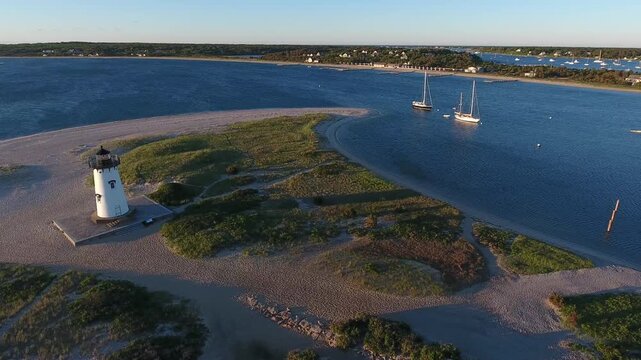 Aerial view of the Edgartown Lighthouse standing tall on a sandy patch surrounded by the deep blue sea and a coastline, Edgartown, Massachusetts, United States.