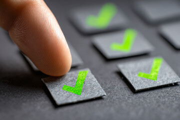 Finger pressing paper checkbox with green checkmark symbolizing task completion and decision making in an organized workflow environment