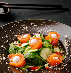 Fresh salmon salad with greens and herbs served in a black bowl