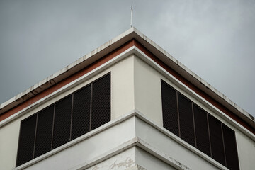 White building corner with ventilation louvers and lightning rod under cloudy grey sky.