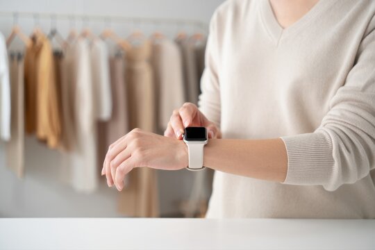 A Person Adjusting a Modern Smartwatch While Dressed in Casual Sweater with Neutral Tones in a Stylish Clothing Store Background
