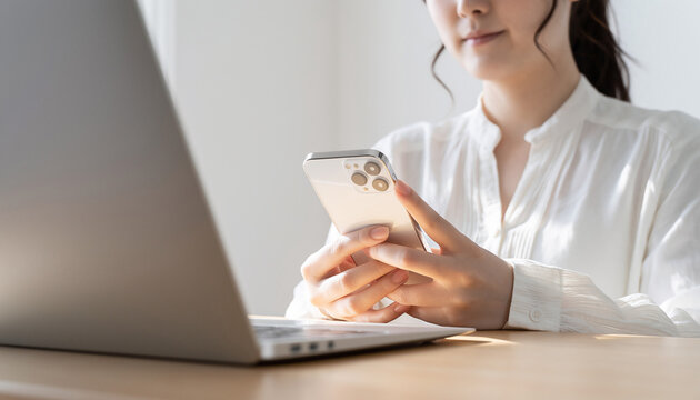 A woman's hand operating a smartphone and a laptop