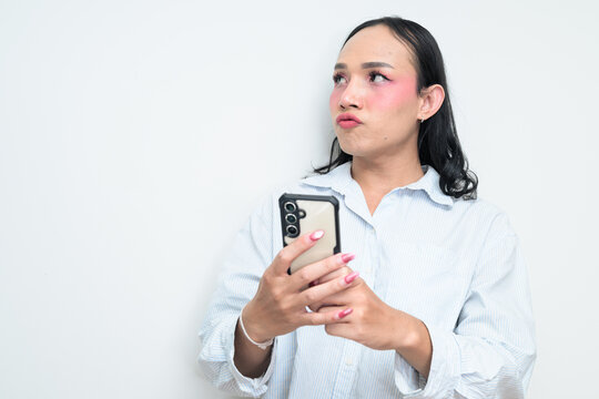Portrait of a young Thai transgender person using phone against white background