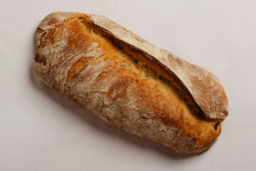 Artisan whole grain pugliese bread with variegated brown crunchy crust, yellow-orange crumb. Neutral white background, soft studio light. Centered composition authentic product.