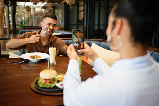 Diverse couple goes photo first in mobile dining, capturing a moment with smartphone, social ritual - Powered by Adobe
