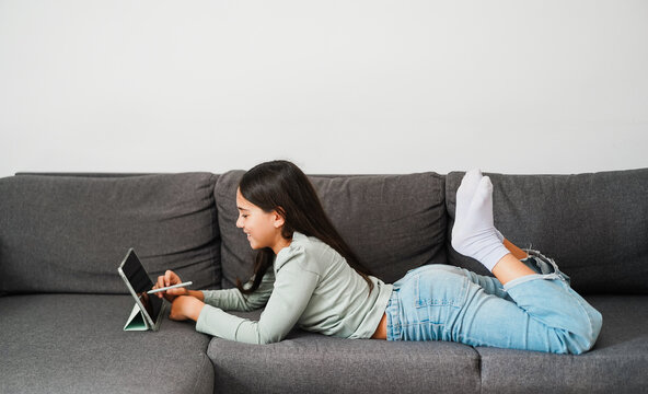 Female teen using tablet while drawing sitting on home sofa - Technology and teenager lifestyle concept - Main focus on face