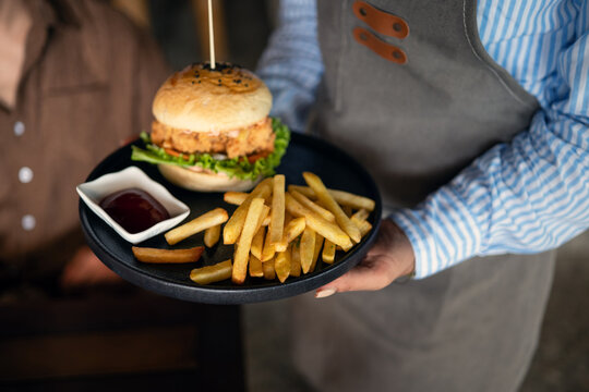 Casual dining lifestyle, waiter serves a delicious burger and fries in a relaxed restaurant setting