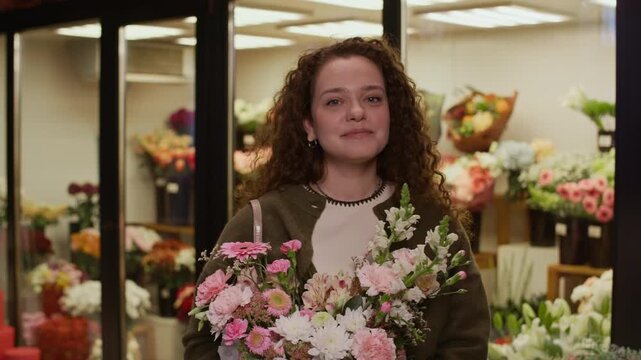 Medium portrait of cheerful Caucasian young woman with bouquet of flowers posing for camera in florist shop - Powered by Adobe