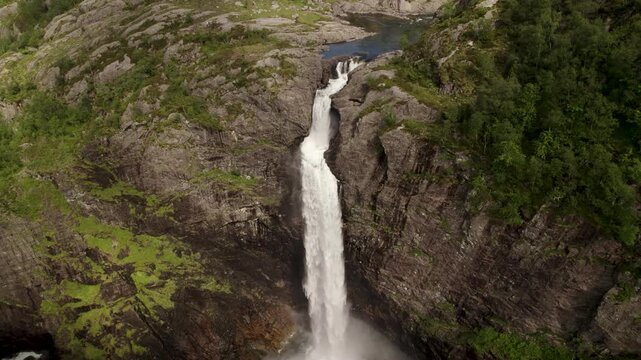 Aerial view of mountains meeting a waterfall and river, with light reflecting off the water, creating a stunning contrast, Dirdal, Rogaland, Norway.