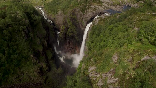 Aerial view of cascading waterfalls plunging into a deep gorge surrounded by dense, vibrant green vegetation, creating a misty spectacle, Dirdal, Rogaland, Norway.