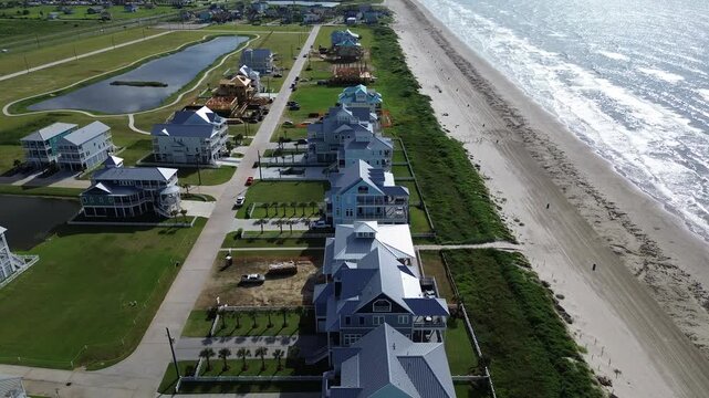 Coastal homes with ocean-facing balconies line beachside road near Sunny Beach, Galveston. Landscaped pond, active construction zone showcase upscale development and shoreline zoning integration