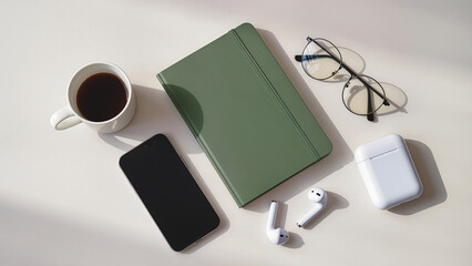 Flat lay composition of green notebook with coffee cup, glasses, smartphone, earbuds, natural daylight, clean background,