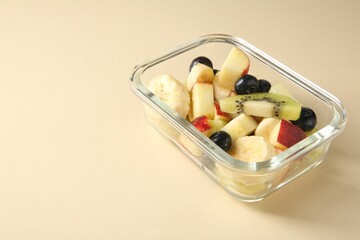 Tasty fruit salad in glass container on beige background, closeup. Space for text