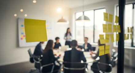 Blurred image of a business meeting in progress, with people around a table and sticky notes on a glass partition