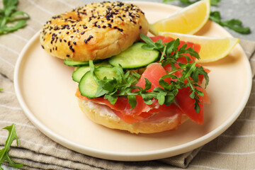 Delicious bagel with salmon, cucumber, arugula and lemon on table, closeup