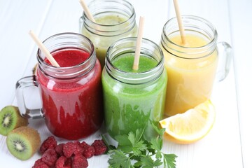 Different tasty smoothies in mason jars and ingredients on white wooden table, closeup