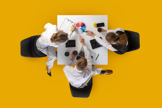 Coworkers pointing at color chart and discussing ideas at white desk in top-down view. Concept of creative teamwork, startup culture, marketing content and education visuals. - Powered by Adobe
