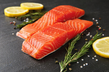 Pieces of salmon fillet, spices and lemon on black table, closeup