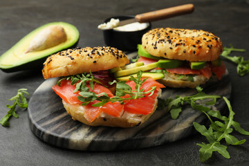 Delicious bagels with salmon, cream cheese, avocado and arugula on black table, closeup