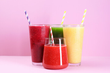 Different tasty smoothies in glasses on pink background