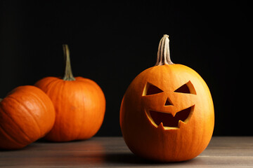 Halloween celebration. Whole and carved pumpkins on wooden table against black background