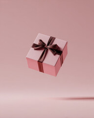 Obraz premium Pink gift box with brown ribbon bow floating against soft pink background conveying celebration and elegance in minimalist composition