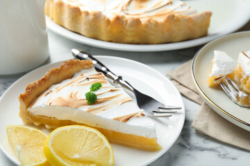 Slice of tasty lemon meringue tart with mint served on white marble table, closeup