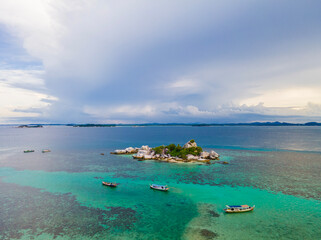 An aerial view of a tropical beach in Belitung, Indonesia. Small boats float on the sea, complementing the composition of clear turquoise blue water and small islands with rocks, white sand, and trees