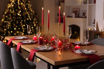 Stylish Christmas table setting with plates, glasses and burning candles in festive decorated room. Bokeh effect