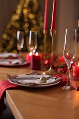 Stylish Christmas table setting with plates, glasses and burning candles in festive decorated room, closeup. Bokeh effect
