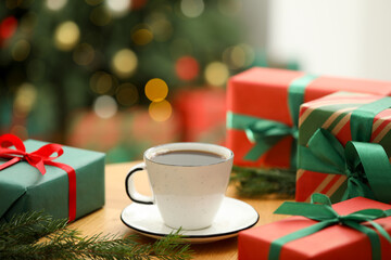 Aromatic coffee in cup, fir tree branches and gift boxes on wooden table against blurred lights,...