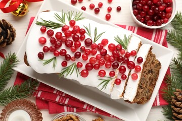 Tasty Christmas cake with icing, cranberries, rosemary and festive decor on white wooden table, flat lay