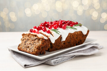 Tasty Christmas cake with icing, cranberries and rosemary on white wooden table against background with blurred lights, closeup