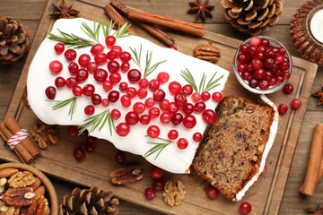Tasty Christmas cake with icing, cranberries and rosemary on wooden table, flat lay