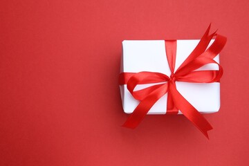 One gift box with ribbon on red background, top view. Space for text