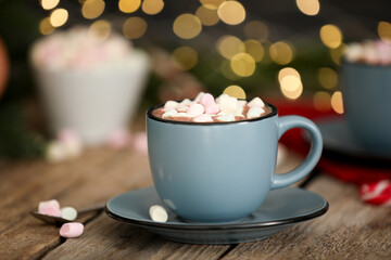 Tasty cocoa with marshmallows on wooden table against blurred Christmas lights, closeup