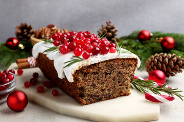 Tasty Christmas cake with icing, cranberries, nuts and festive decor on light grey table, closeup