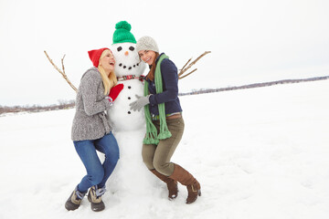 Women, friends and laugh with snowman outdoor for Christmas, snow activity and bonding on holiday....