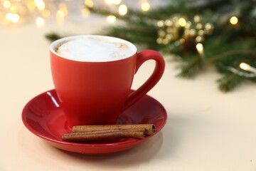 Aromatic coffee in cup, cinnamon and Christmas decor on beige background, space for text. Bokeh effect