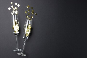 Merry Christmas and Happy New Year. Flute glasses with golden star shaped confetti on black...