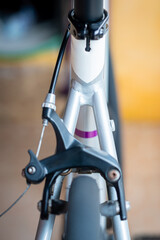 A close-up shot of a black bicycle road caliper brake mounted on a silver frame, showing the brake cable, wheel, and tire