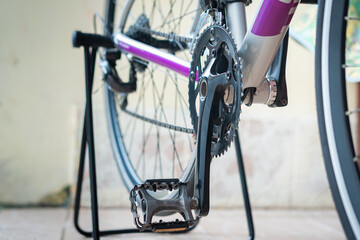 Close-up of a bicycle crankset and pedal on a repair stand, highlighting metal gears and chain details in a clean indoor setting