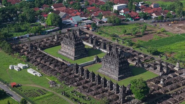 Aerial view of the ancient Candi Plaosan temple complex with its dark stone structures contrasting against the lush green grass, Klaten Regency, Jawa Tengah, Indonesia.