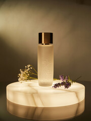 Studio product shot of a sleek glass perfume bottle placed on a round marble podium, illuminated with soft warm light. Clean, minimal, elegant composition ideal for luxury branding.