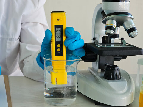 Scientist measuring pH level with digital meter near a microscope in laboratory