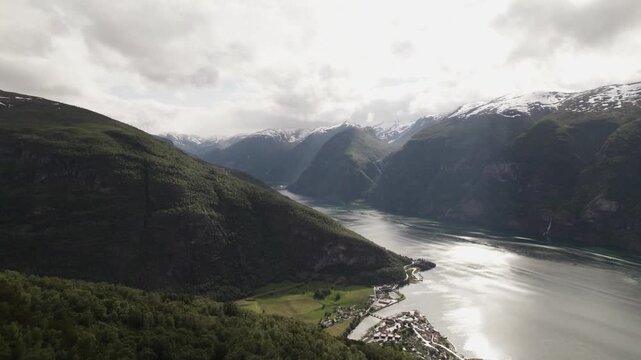Aerial view of a stunning landscape with a fjord reflecting sunlight, surrounded by dark mountains partially covered in snow, Aurland, Vestland, Norway.