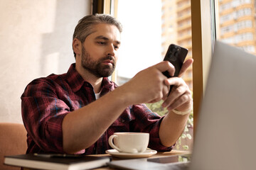 Handsome mature man enjoys coffee while engaging with his smartphone at a stylish café