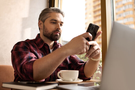 Handsome mature man enjoys coffee while engaging with his smartphone at a stylish café