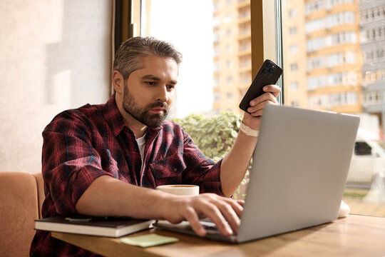 Mature man wearing stylish attire engages in work while enjoying coffee at a cozy cafe - Powered by Adobe